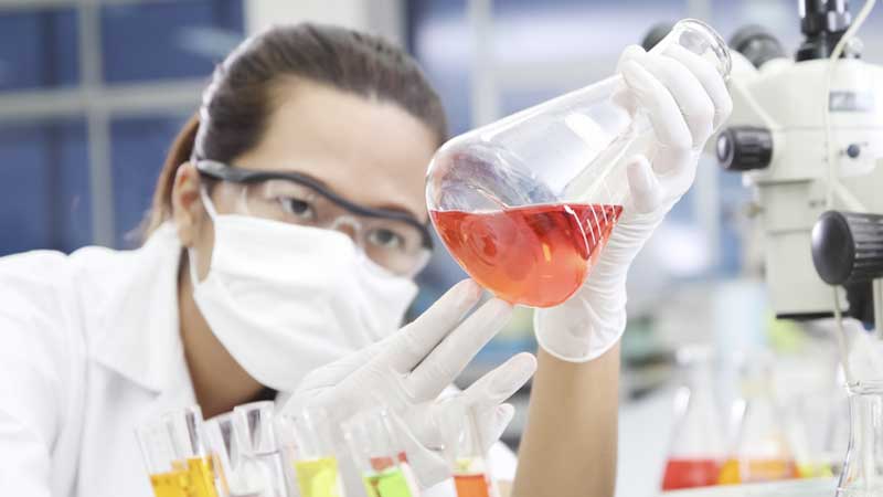 A laboratory scientist who works with New Orleans, LA based Tarun Jolly, M.D. holding up a beaker containing orange fluid